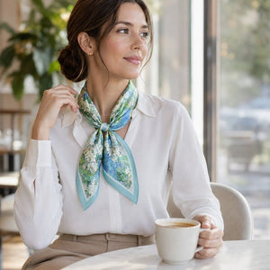 Woman sitting at a table with a cup of coffee, wearing a floral scarf.